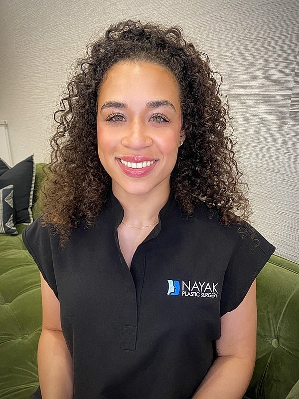 Smiling professional in plastic surgery attire.