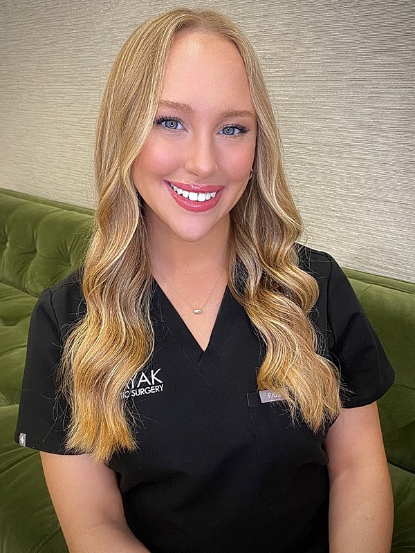Smiling woman in medical attire against green background.