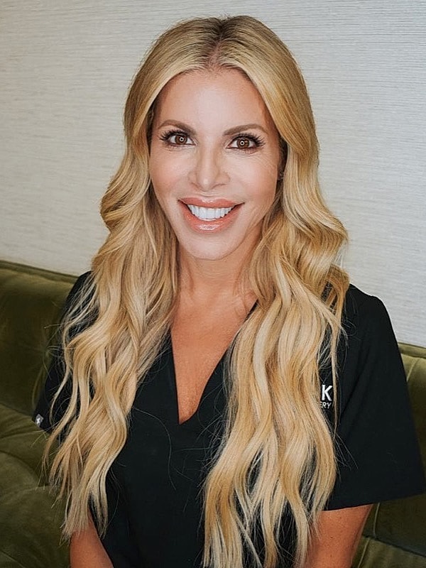 Smiling person in professional attire with wavy hair.