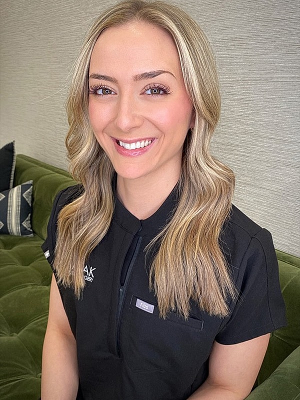 Smiling woman in medical attire against green background.