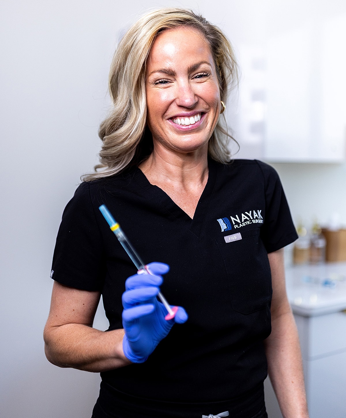 Smiling St. Louis Cheek Filler professional holding a syringe in clinic.