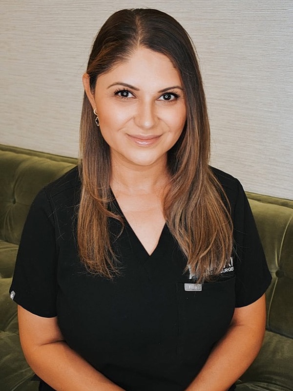 Smiling woman in medical attire seated on couch.