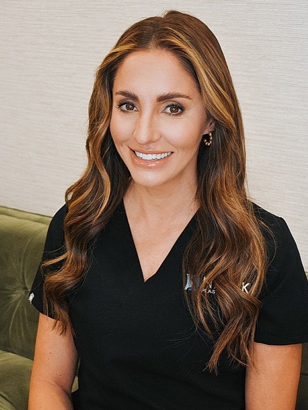 Smiling woman in medical scrubs, seated indoors.