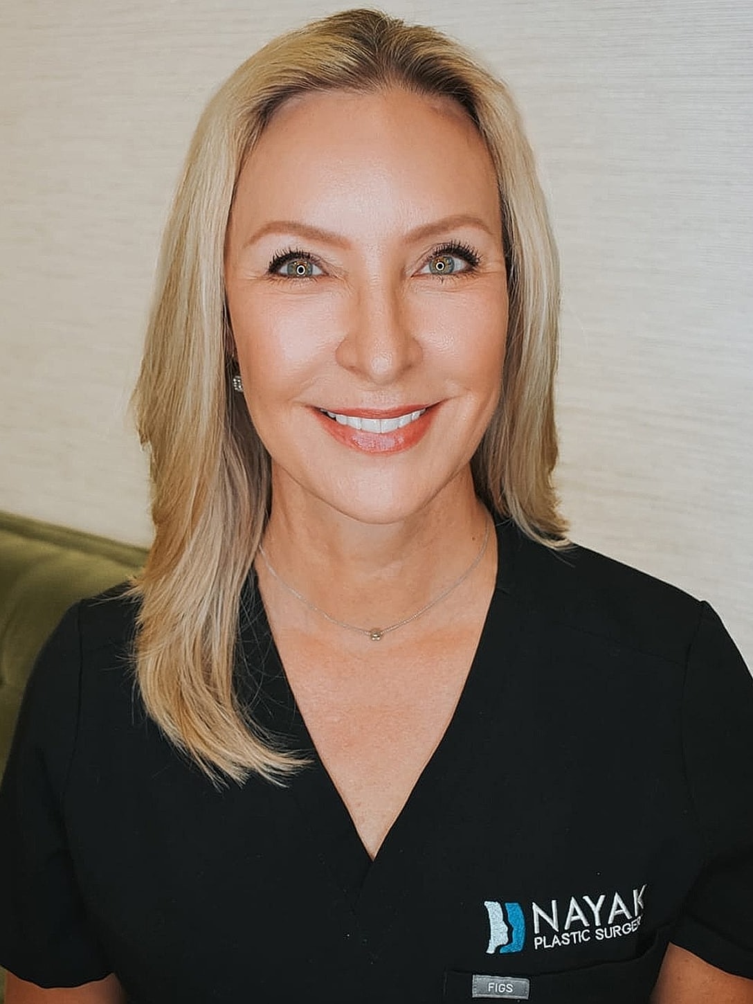 Smiling woman in medical attire at plastic surgery office.