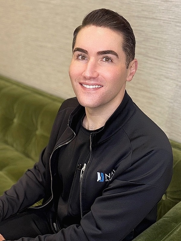 Smiling man in black jacket sitting on couch.