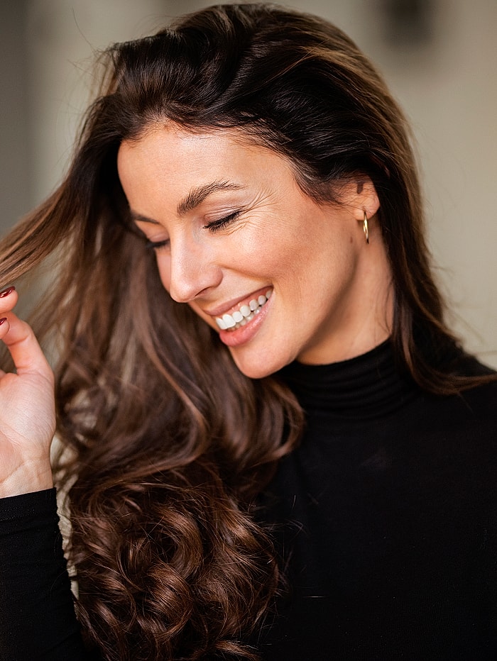 Smiling woman touching her hair in black outfit.