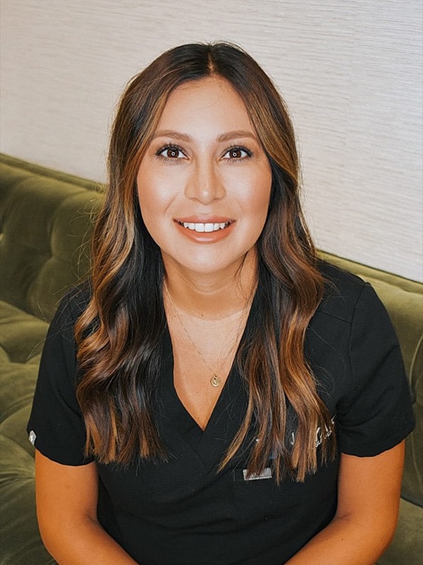 Smiling woman in medical scrubs, seated on couch.